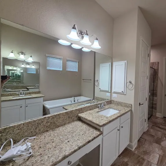 Bathroom with beige walls, white cabinets, granite countertops, and a large mirror