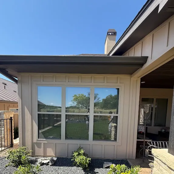 Beige exterior siding with white window trim beneath a dark roof edge