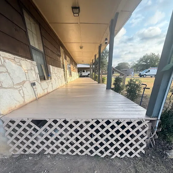 Covered wooden porch with gray floorboards, painted posts, and white lattice skirting