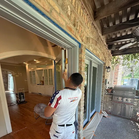 Painter working on exterior trim around a sliding glass patio door beside stone siding