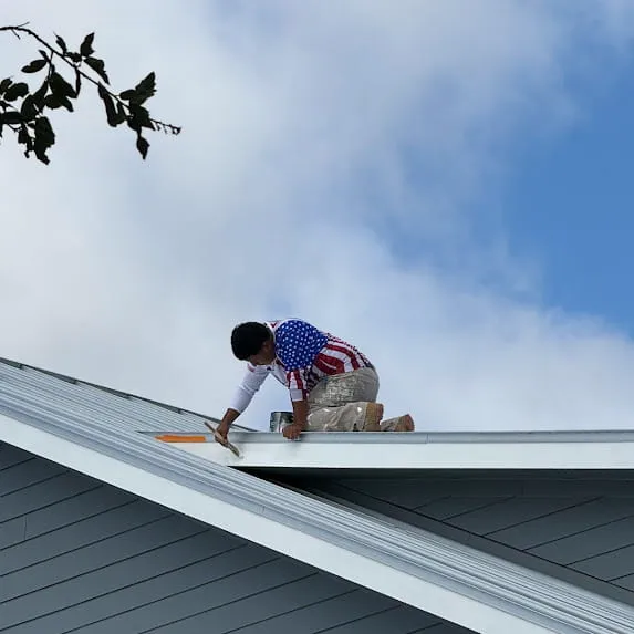 HOME 93 Painter working on white exterior roof trim above gray house siding