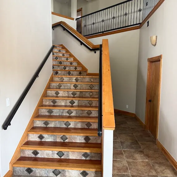 Staircase with light painted walls, natural wood trim, and a black handrail