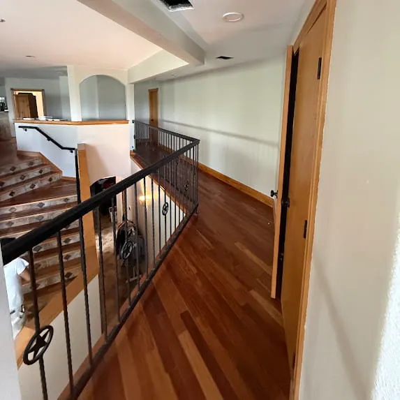 Upstairs hallway with light painted walls, natural wood door trim, and black stair railing