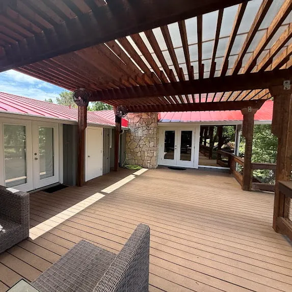 Wooden deck beneath a dark stained pergola beside gray exterior siding and white doors