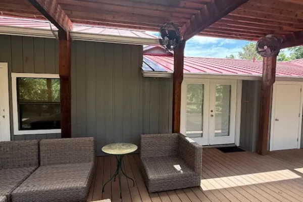 Covered deck with dark stained wood beams, gray exterior siding, and white door trim