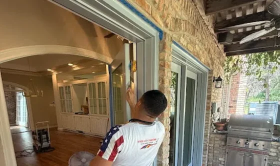 Painter working on exterior trim around a sliding glass patio door beside stone siding