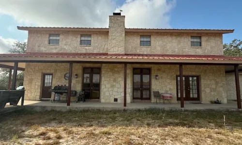 Two-story stone house with a covered rear porch and dark painted posts and trim